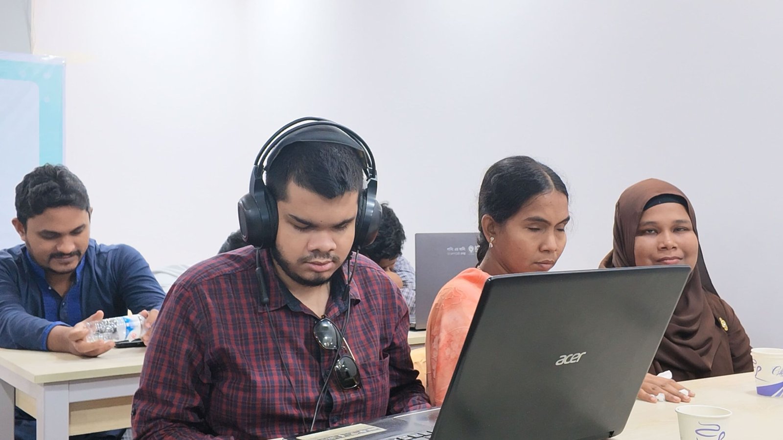 A visually impaired young man wearing headphones conducting live WCAG accessibility audit testing on a laptop with fellow participants