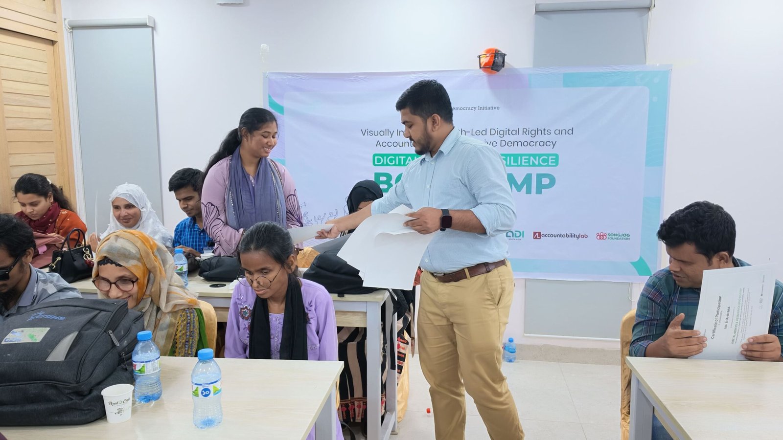 Project coordinator presenting accessibility auditor certificates to youth participants with disabilities in front of the Digital Rights Bootcamp banner
